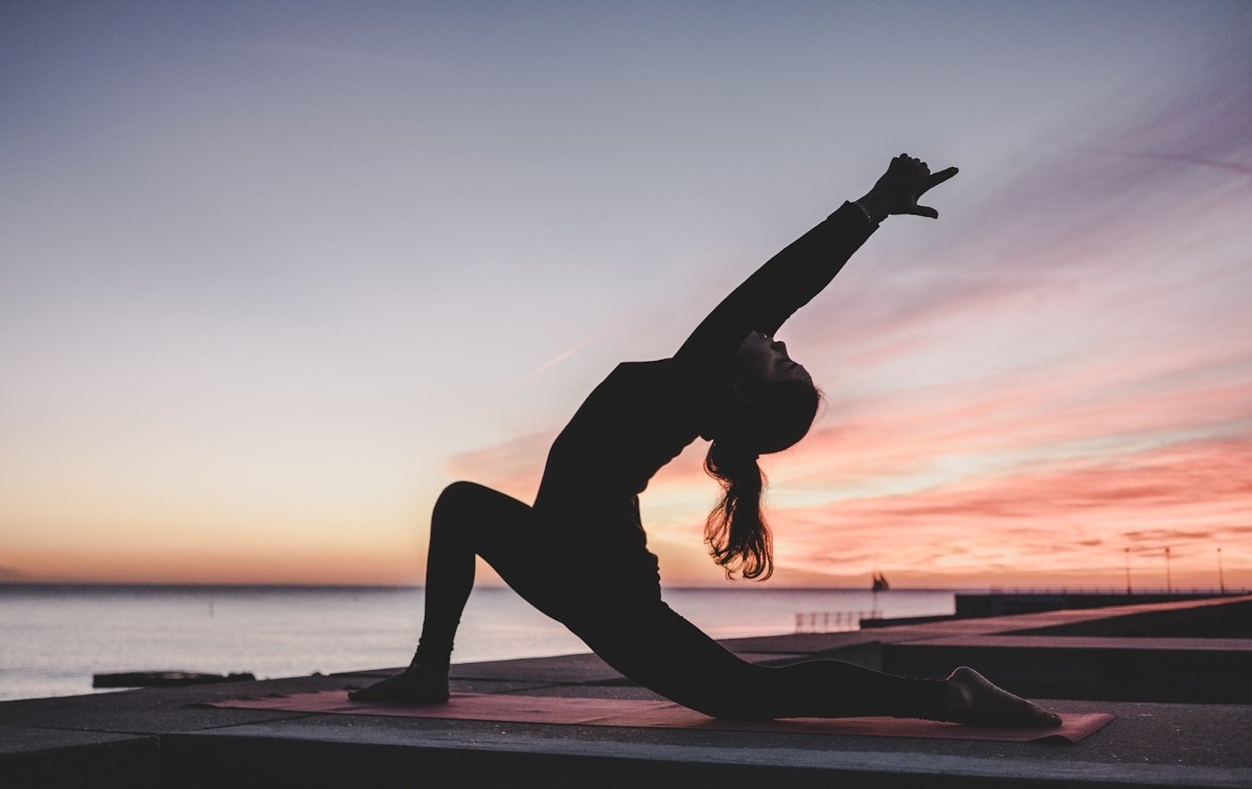 A woman stretching in morning light — daily wellness routine with a glass of water by a bright window